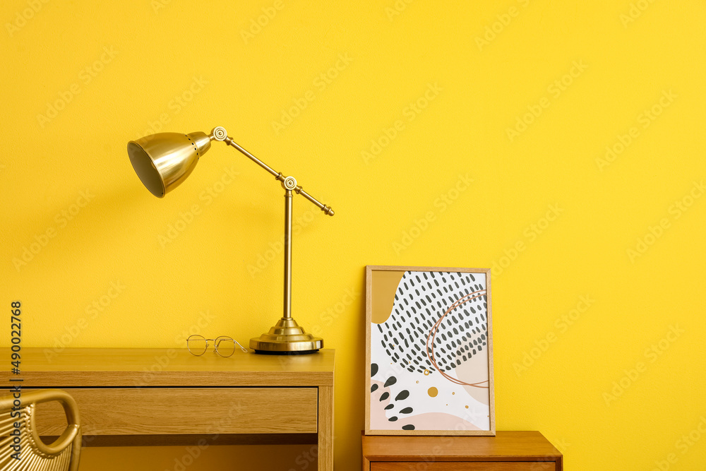 Wooden desk with golden lamp near yellow wall