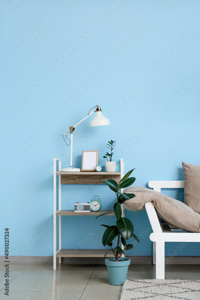 Comfortable sofa, houseplants and modern lamp on table near blue wall