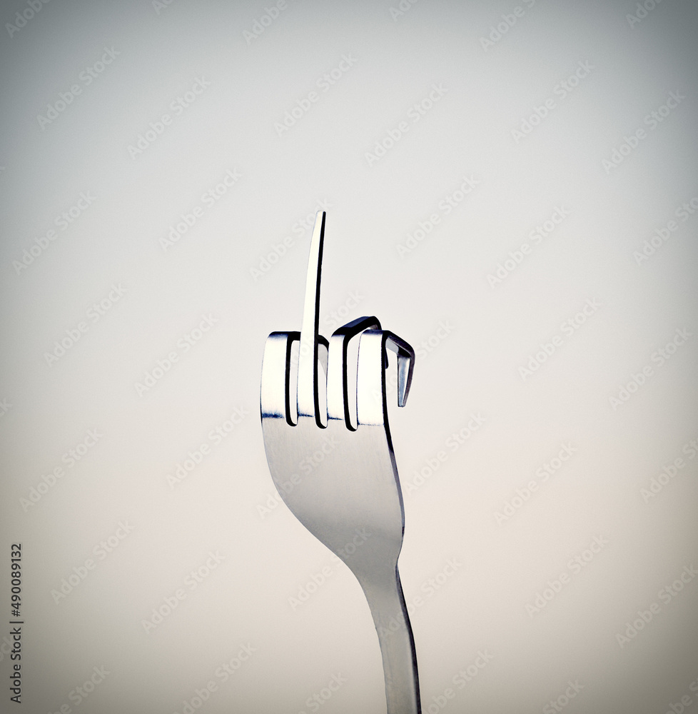 用叉子叉你。一把叉子在灰色上孤立时表现出粗鲁的手势。