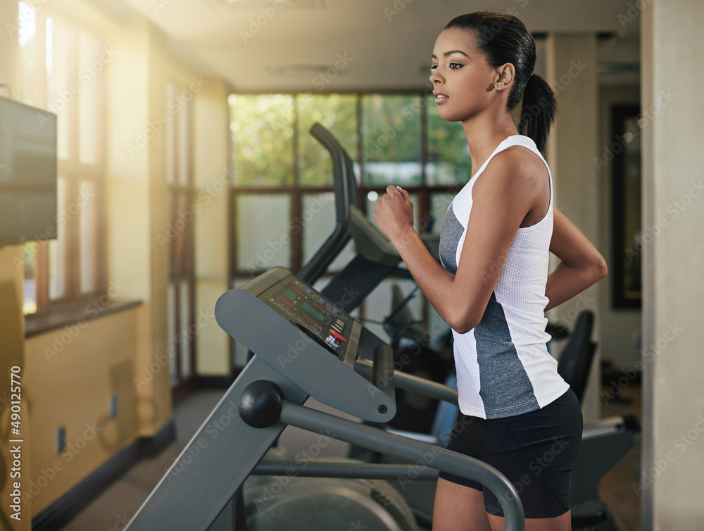 在跑步机上汗流浃背。一名年轻女子在健身房的跑步机上锻炼的照片。
