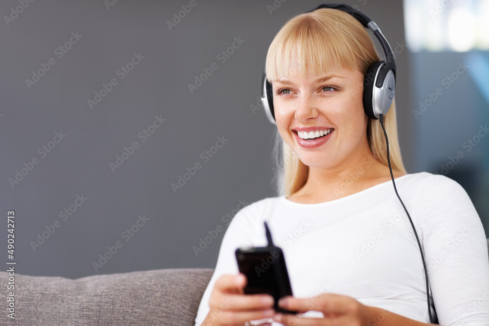 音乐爱好者。微笑的年轻女子通过MP3播放器听音乐的特写。