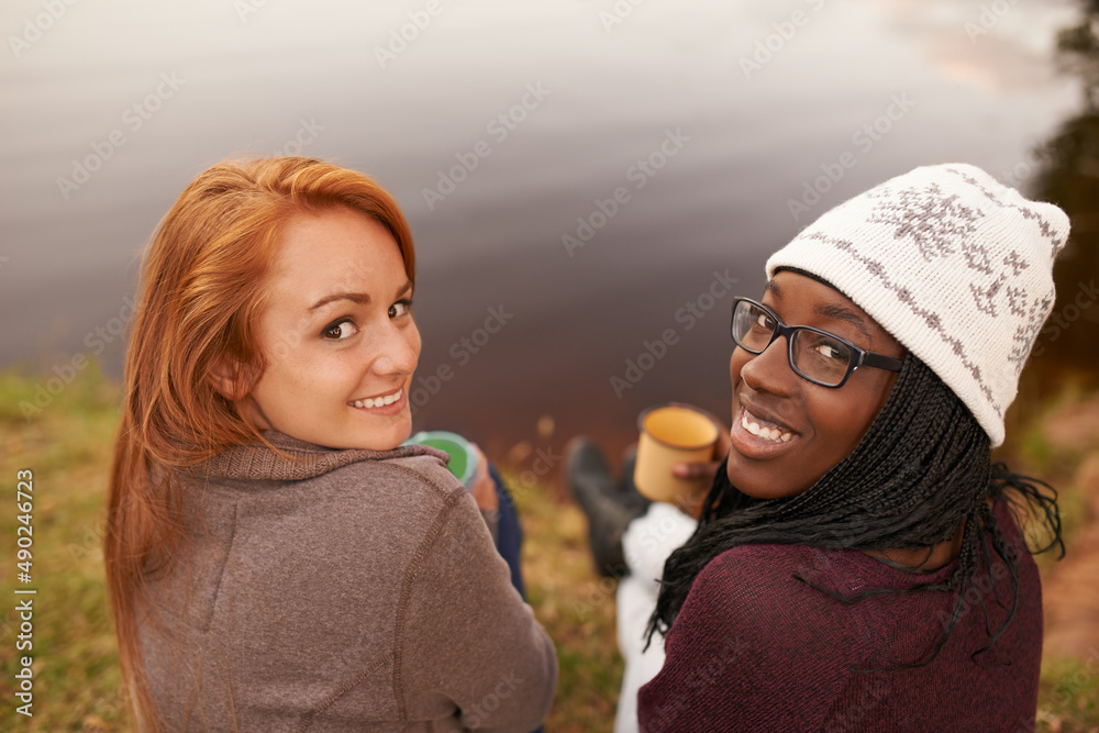Winter outings to the lake. High angle portrait of two happy teenage girls sitting beside a lake.