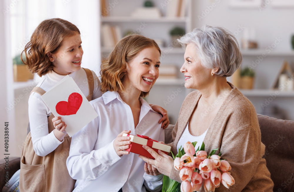 国际妇女节快乐。微笑的女儿和孙女向奶奶送鲜花和礼物