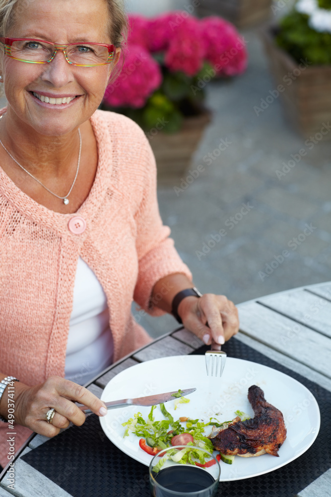Meat fresh off the BBQ. A senior woman enjoying a delicious meal outdoors in the evening.