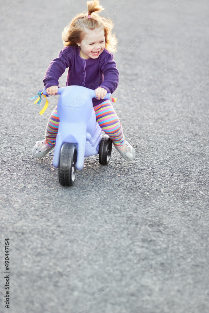 骑着三轮车玩得很开心。一个可爱的女婴骑着三轮车在外面的街上。