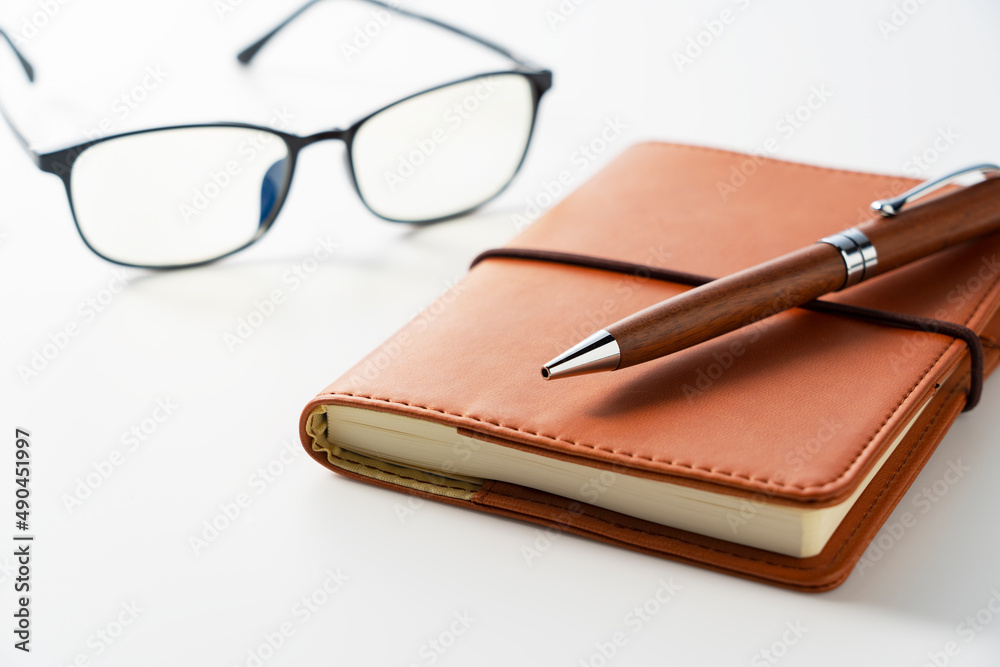 白色背景上的皮革笔记本、钢笔和眼镜。