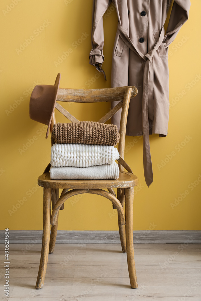 黄色背景挂毛衣、帽子和风衣的木椅