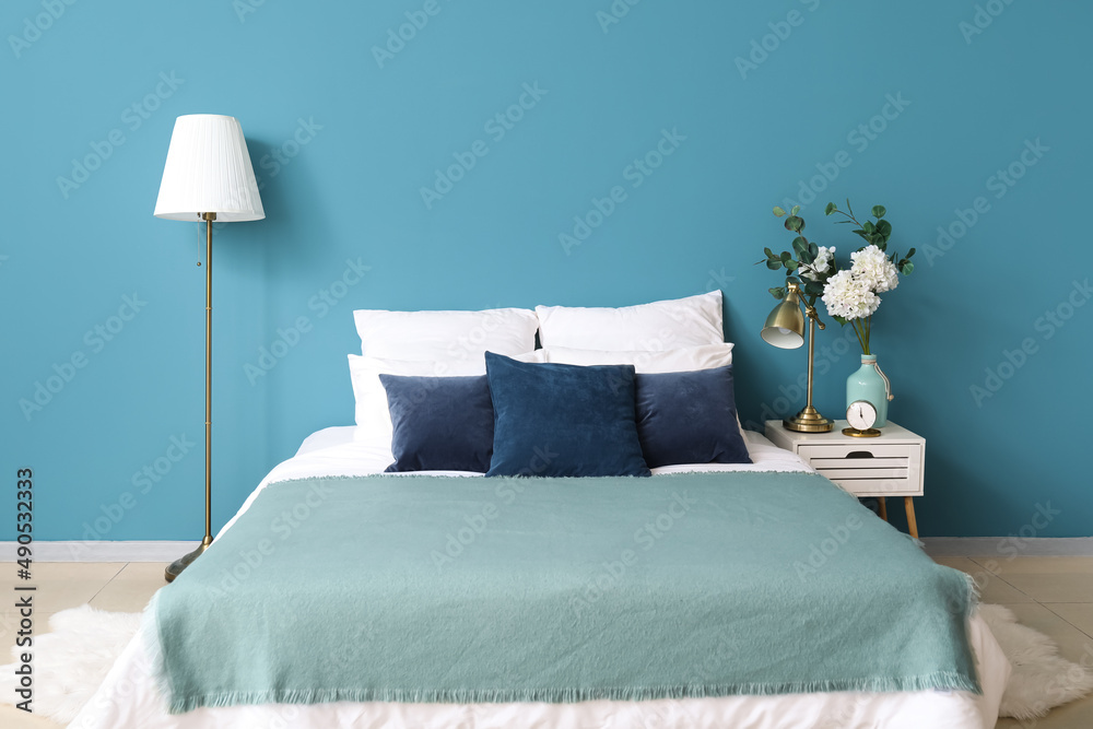舒适的床，床头柜上的花瓶，蓝色墙壁附近的现代灯
