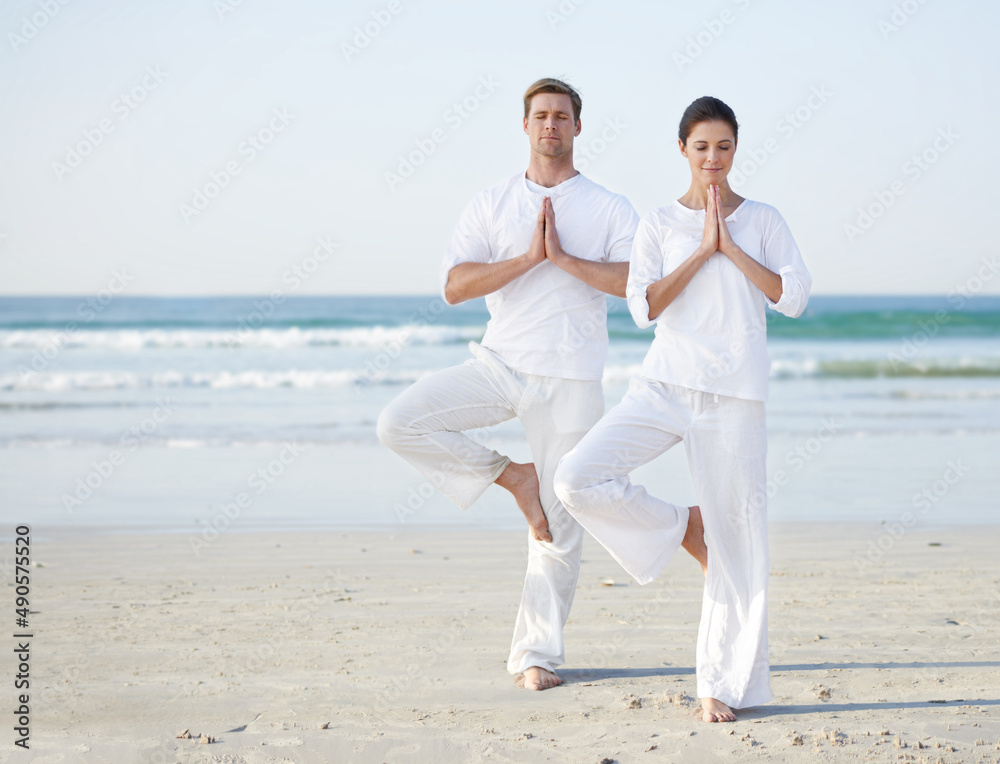 海边瑜伽。一对年轻夫妇在海滩上练习瑜伽。