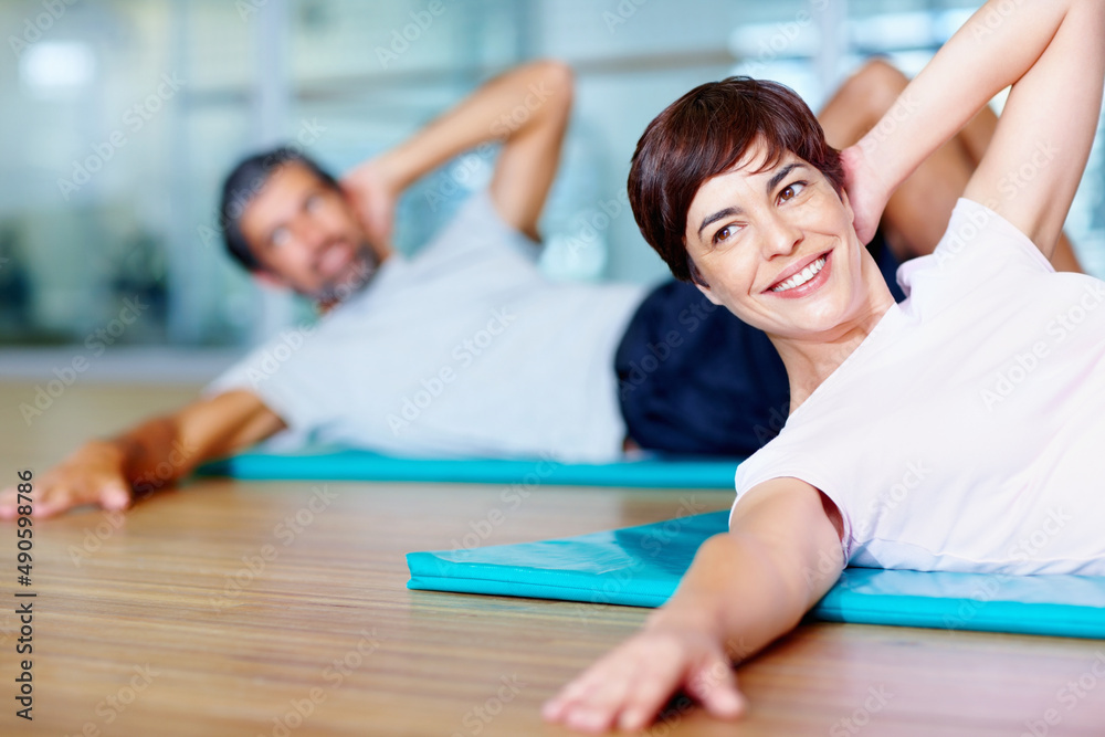 美丽的女人在锻炼。快乐的女人和男人在健身房的瑜伽垫上锻炼。