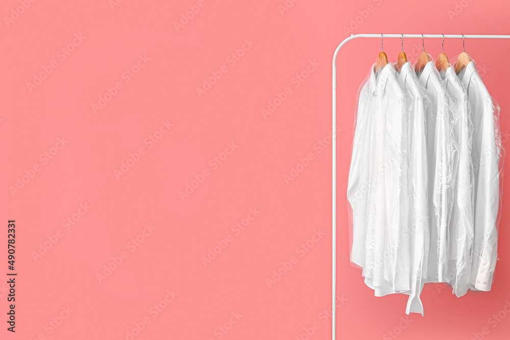 粉红色背景的塑料袋里装着干净的白衬衫的架子