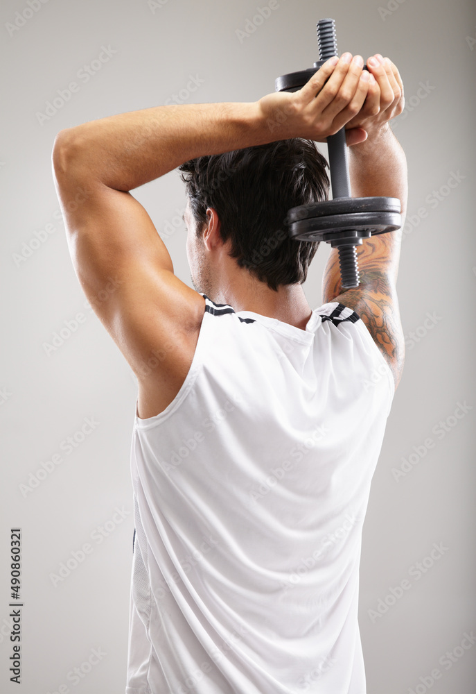 Working those biceps. Rearview of a young man using dumbbells to strengthen his triceps.