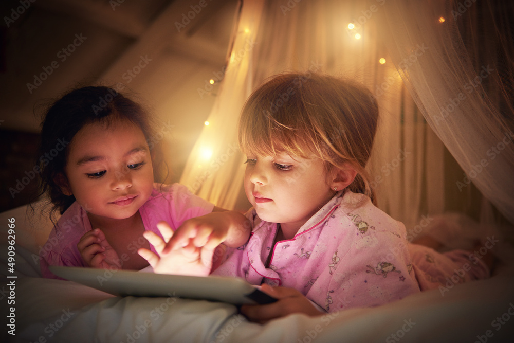 Its time for some bedtime magic. Shot of two little girl using a digital tablet at their sleepover.