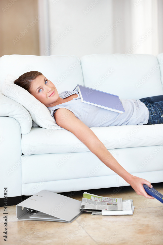 Taking a much needed study break. Smiling young student lying on the sofa with all her books.