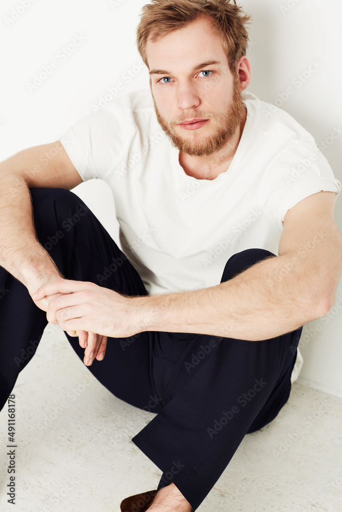 Hes got a casual style. Portrait of a young man sitting on the floor against a wall.