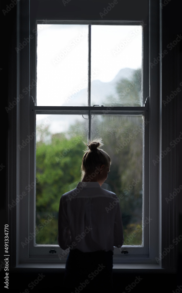 Room with a view. A beautiful young woman standing by a window.