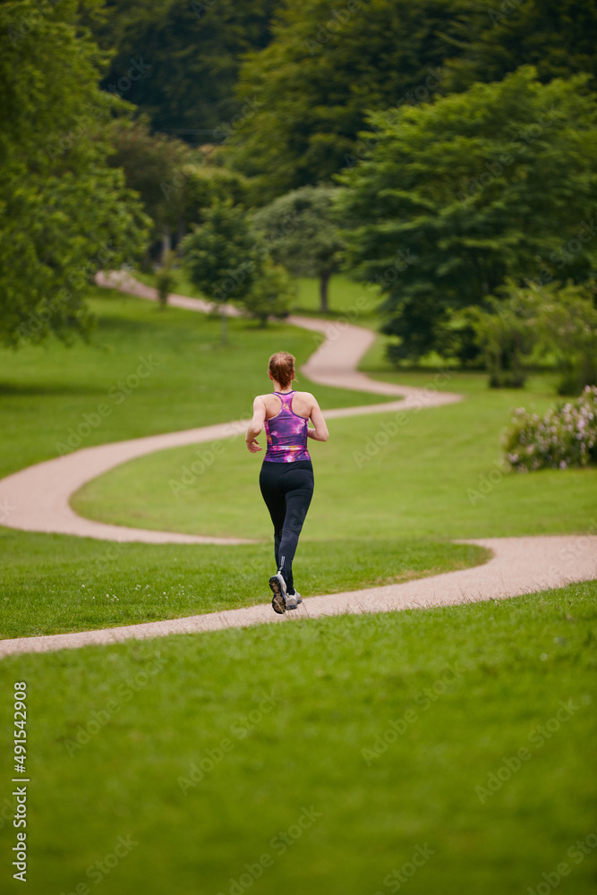 穿着它进行长跑。一名女子在公园的人行道上慢跑的后视镜头。