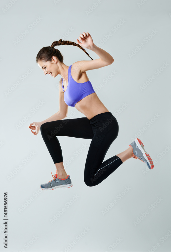 Go beyond your limit. Side view shot of a sporty young woman jumping against a gray background.