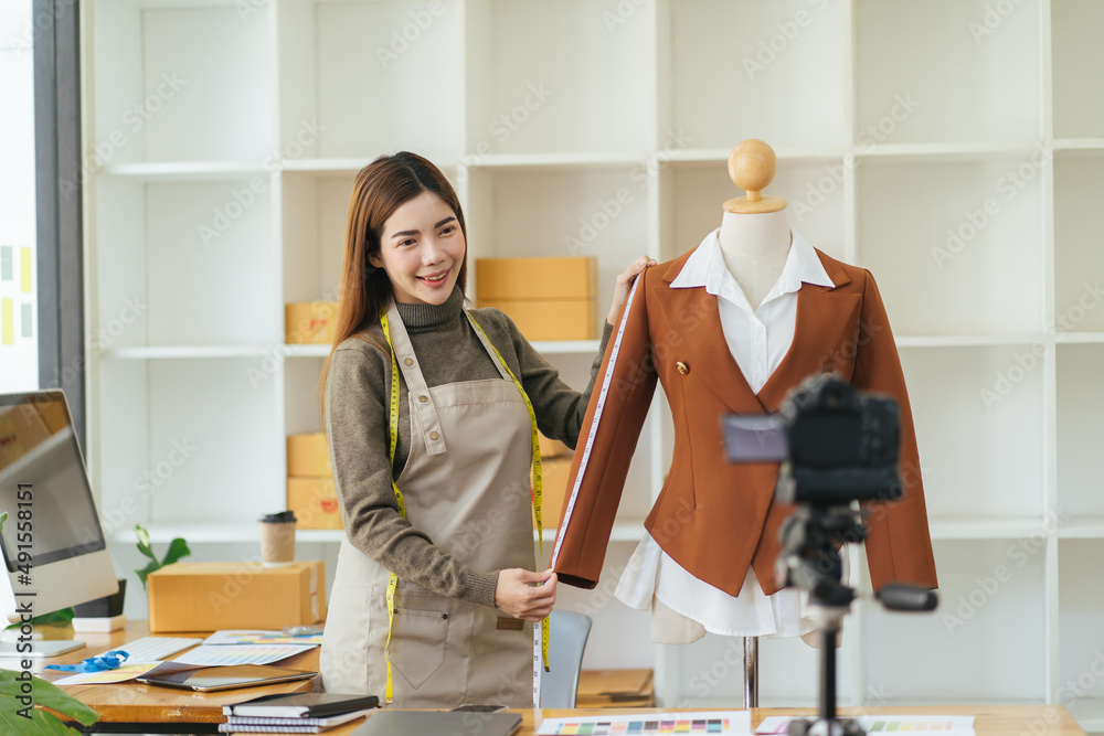 Young Asia lady fashion designer using mobile phone receiving purchase order and showing clothes rec