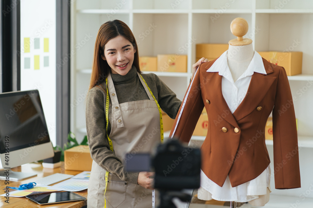 Young Asia lady fashion designer using mobile phone receiving purchase order and showing clothes rec