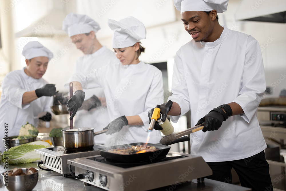 身着制服的多种族专业厨师团队在厨房为餐厅做饭。L