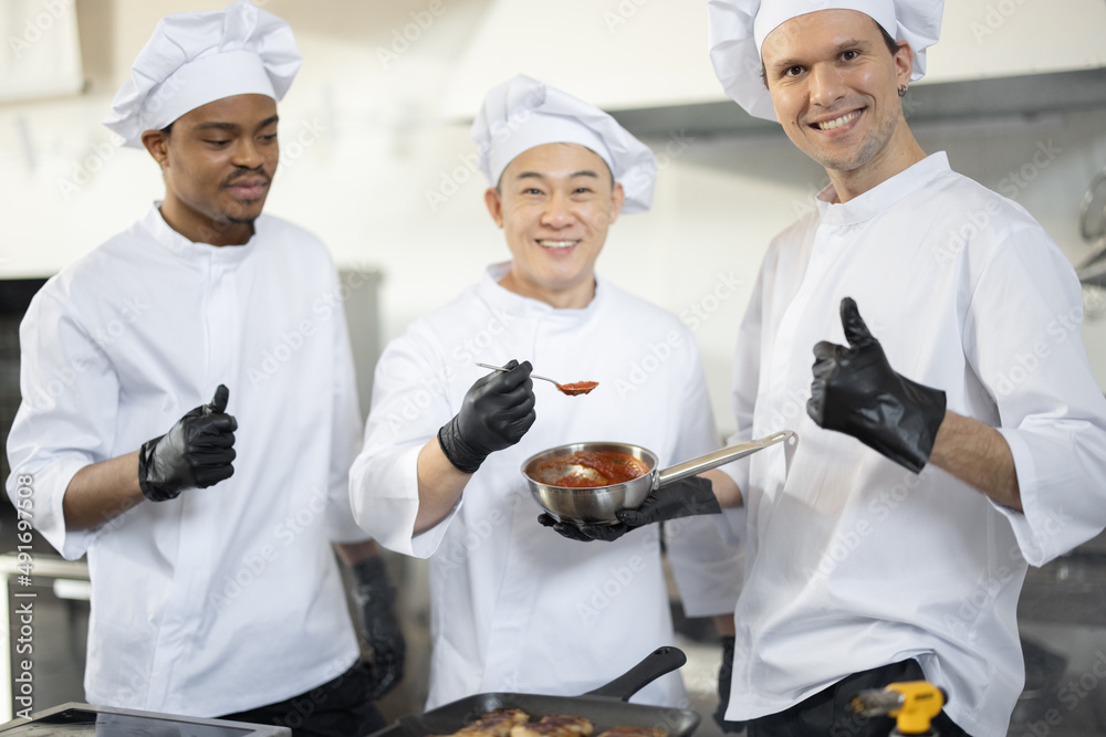 三位不同种族的厨师在餐厅烹饪时拿着装有酱汁的锅的肖像