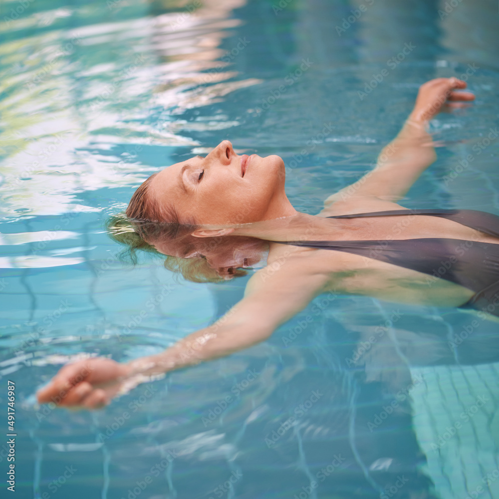 让她的压力消散。一位成熟女性在室内游泳池放松的裁剪镜头。