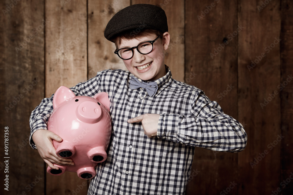 Saving is what its all about. Young boy in retro clothing holding his piggybank while pointing towar
