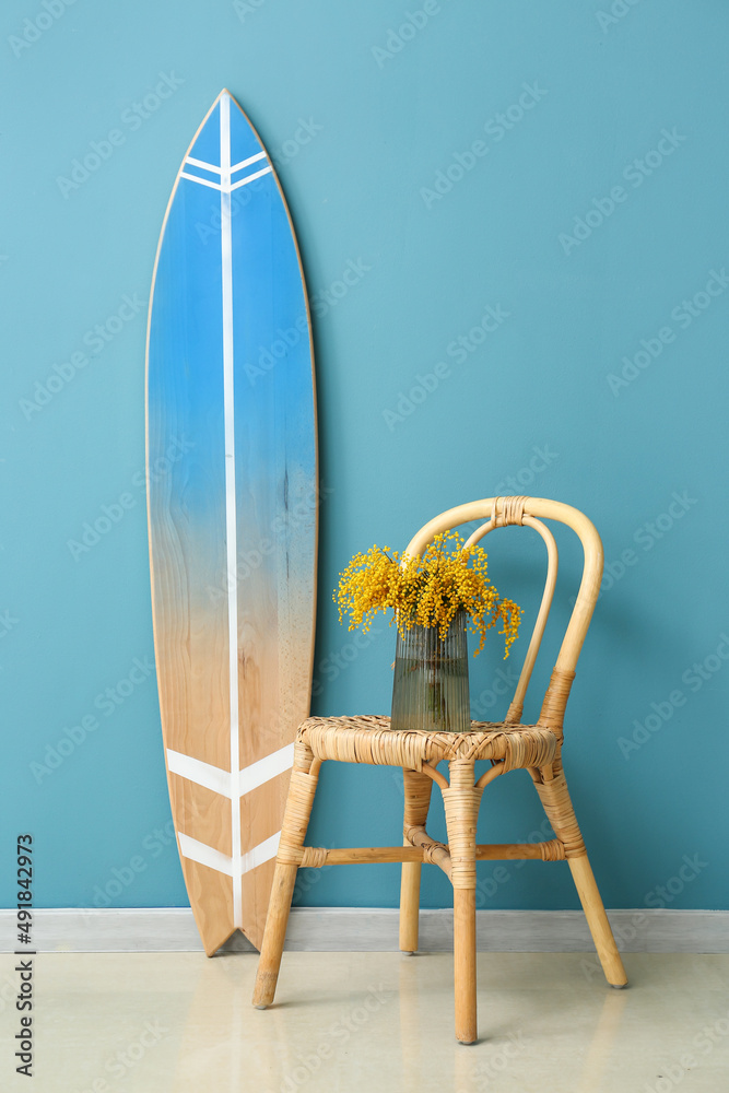 房间彩色墙壁附近的椅子和冲浪板上有含羞草花的花瓶