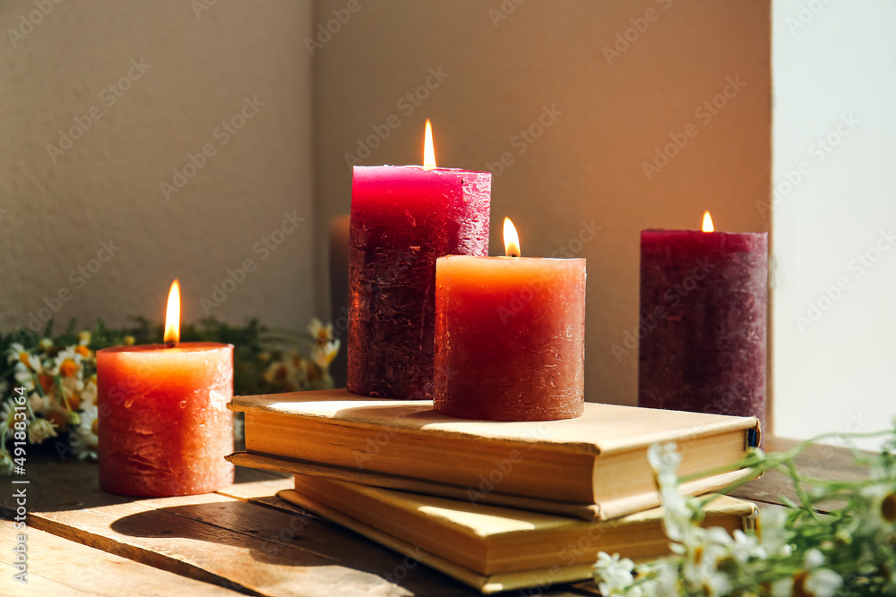 Burning candles with books on wooden table