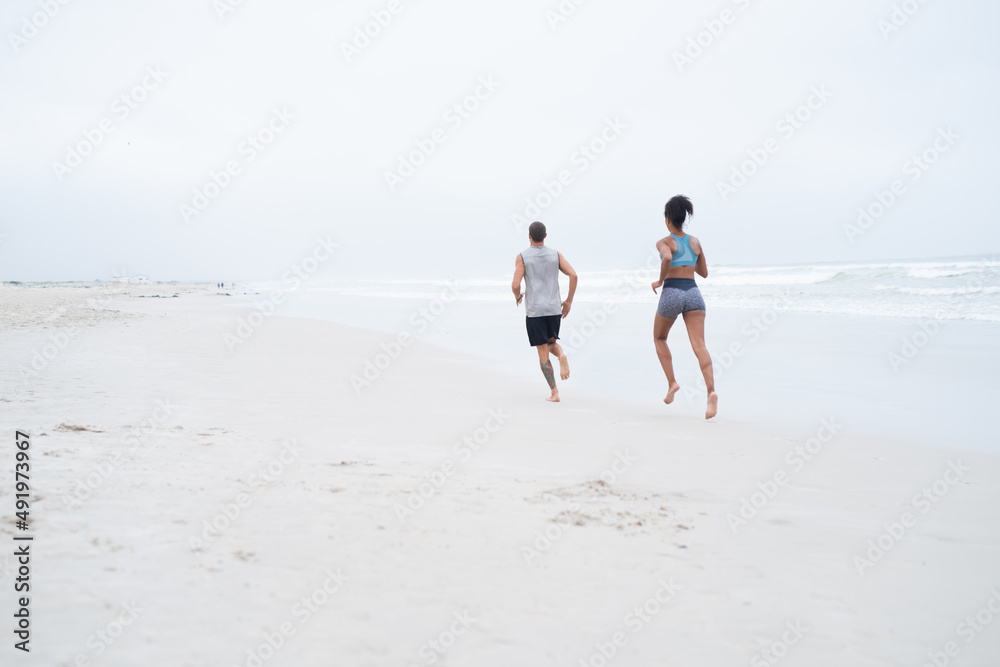 让他们的海滩身体为夏天做好准备。一对年轻夫妇在海滩上奔跑的后视镜头