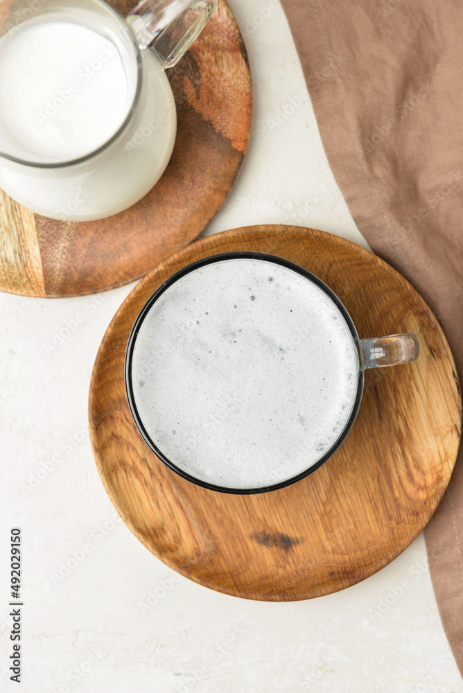 Wooden plate with glass cup of Charcoal Latte and jug with milk on light table