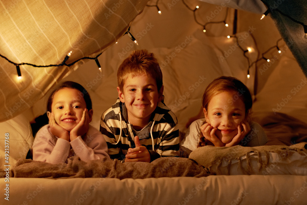 This is our blanket fort. Shot of three young children in a tent together.