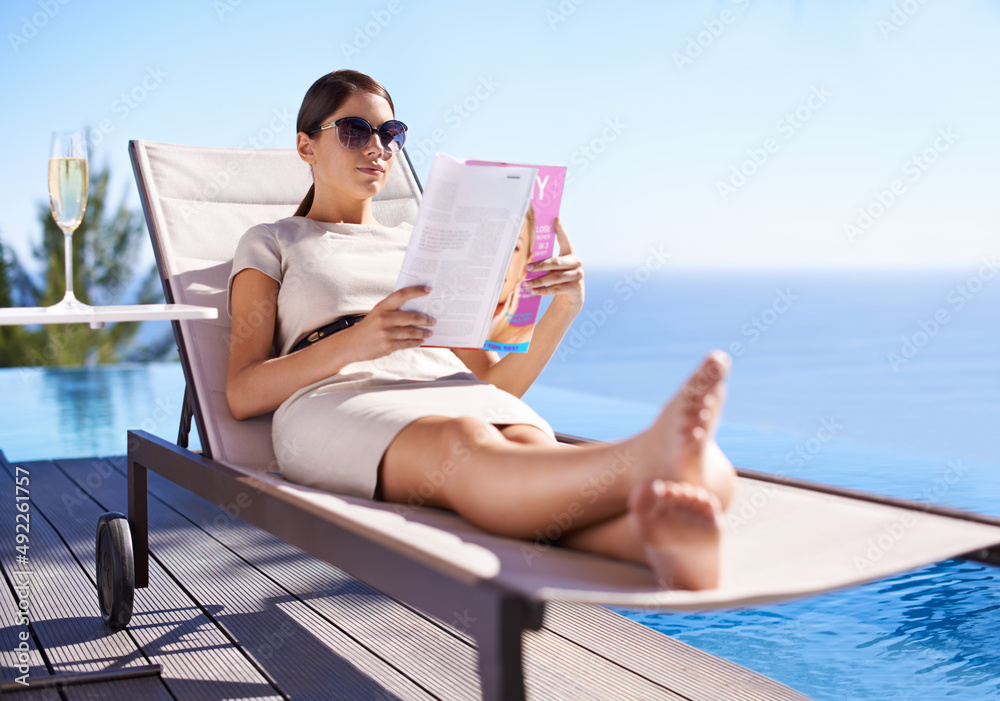 享受假期。一位迷人的年轻女性躺在躺椅上看杂志。