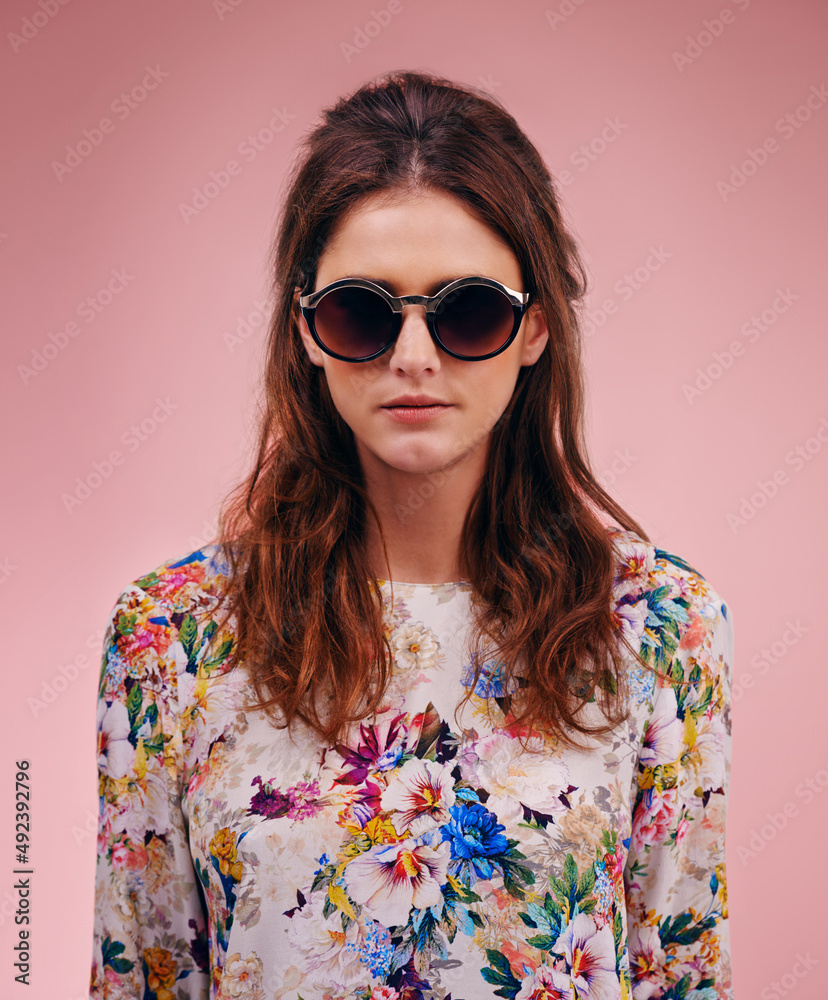 Stunning and stylish. Portrait of an attractive young woman wearing designer shades against a pink b