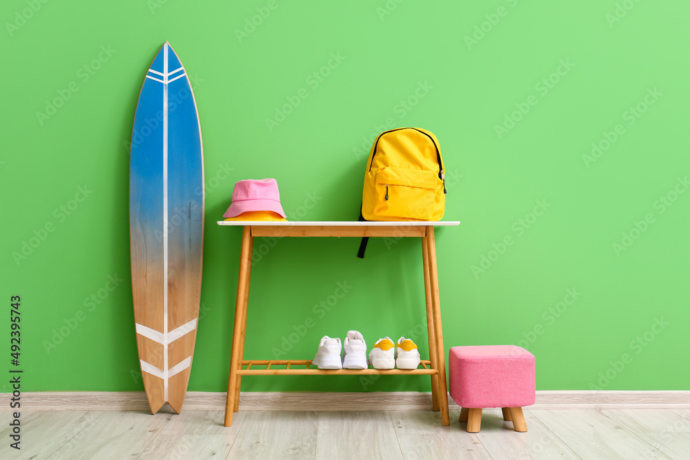 房间里靠近绿色墙壁的桌子上有背包、帽子、鞋子和冲浪板