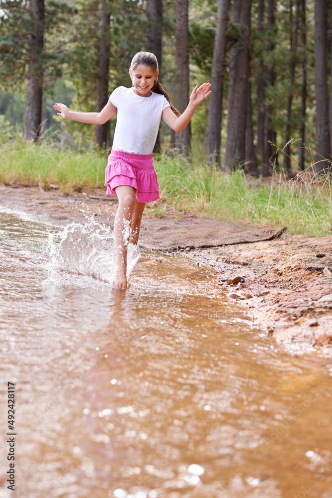 Splashing around is so much fun. A cute little girl running through a wilderness stream.