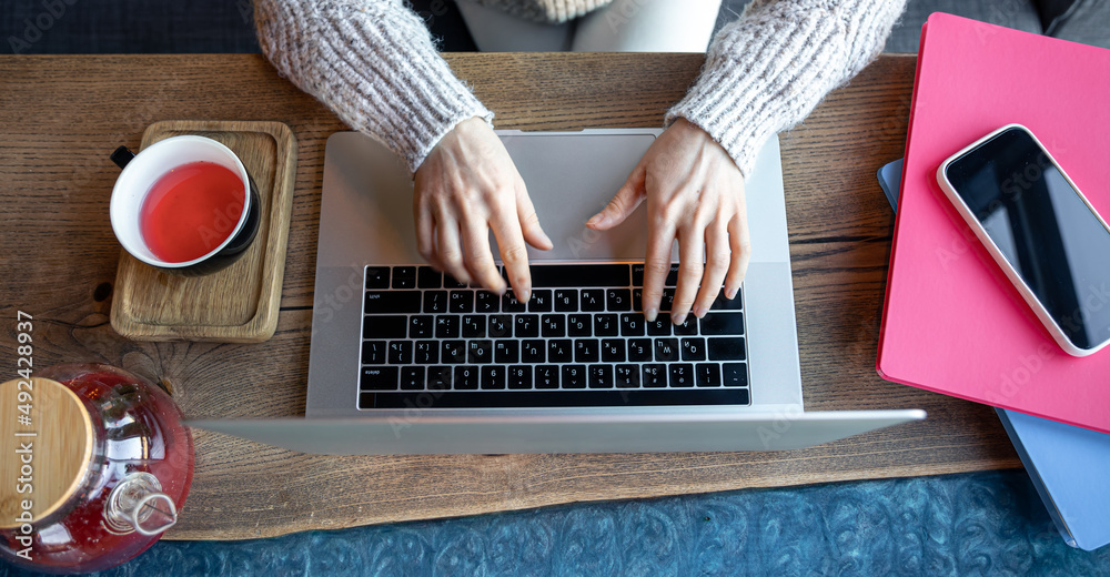 一位女士在咖啡馆用笔记本电脑工作，喝杯茶，俯视图。