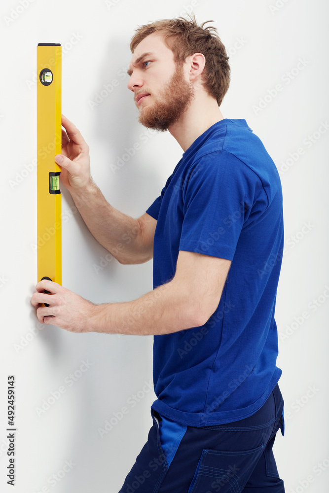 Making sure the wall is level. An unshaven young man using a level to make sure the wall is straight