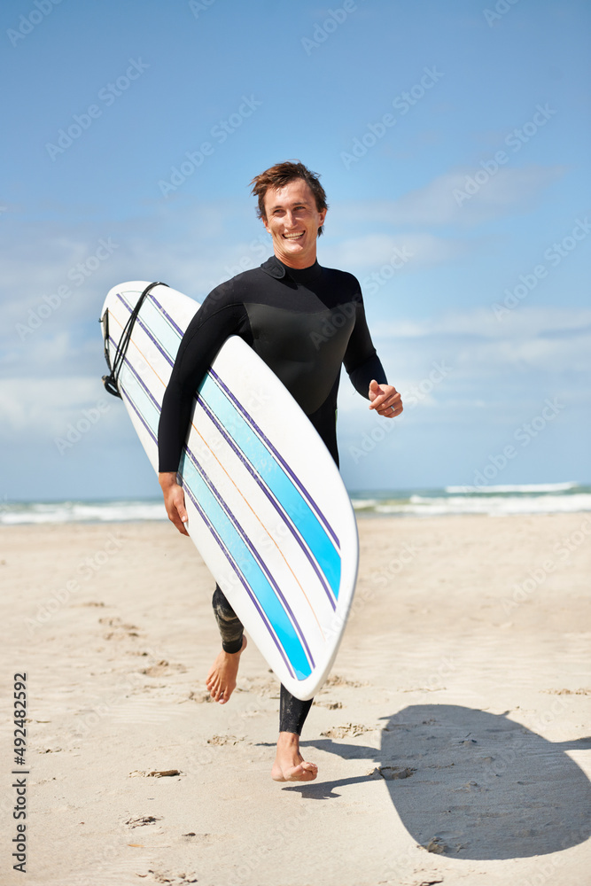 冲浪精神。一个英俊的冲浪者拿着冲浪板在海滩上奔跑。