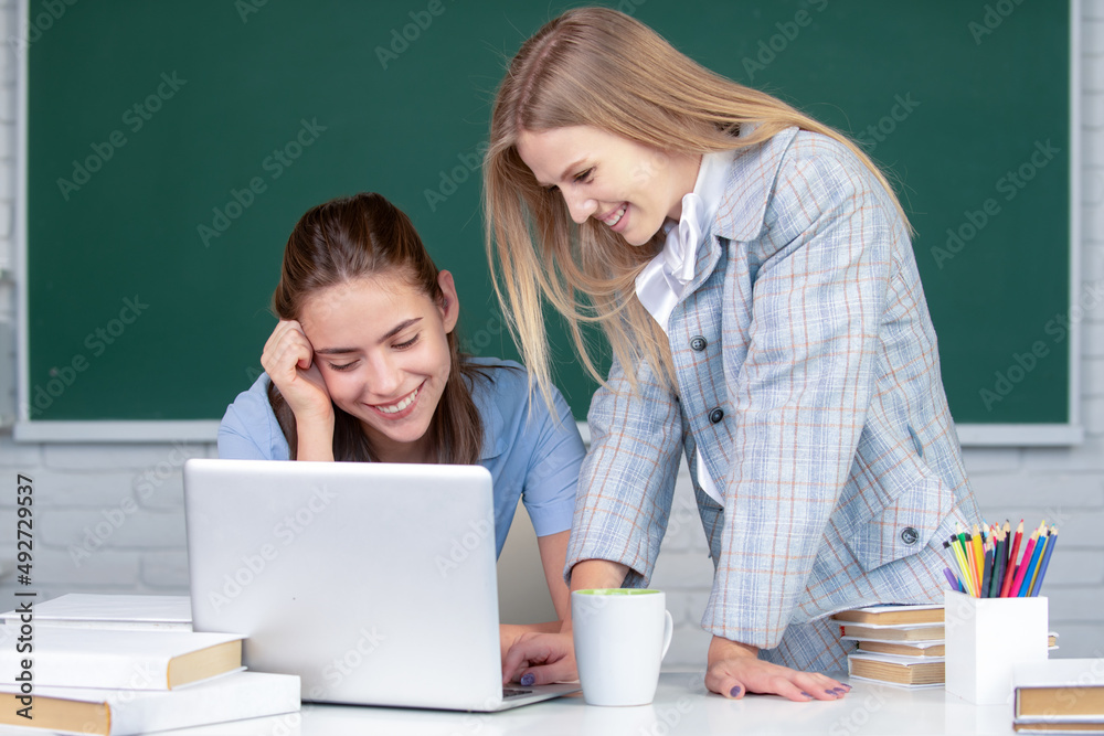 在学校里，女孩们在教室里看着笔记本电脑。两个学生在做家务
