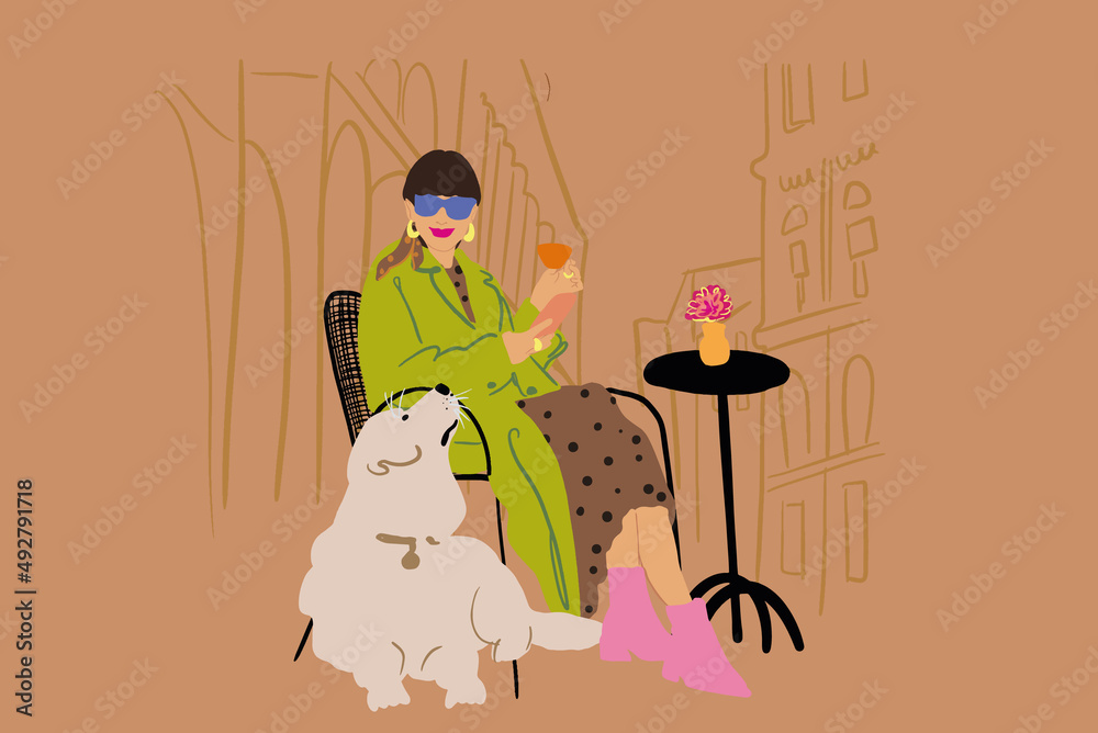 年轻时尚的女人和她的狗坐在城市背景下的咖啡馆露台上喝鸡尾酒。