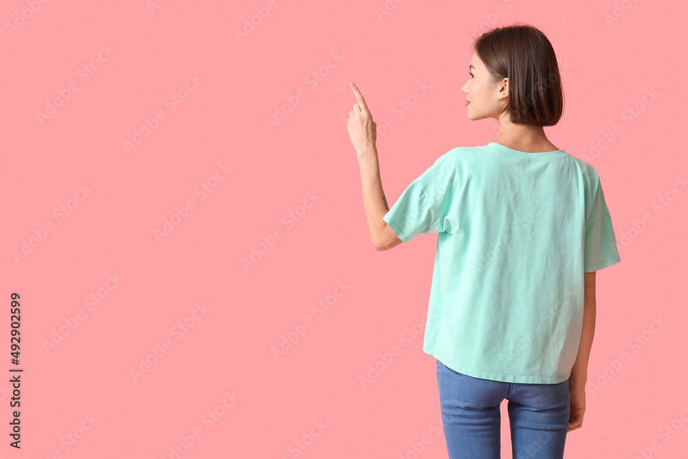 穿着时尚t恤的漂亮年轻女性，在彩色背景下指着某个东西，背影