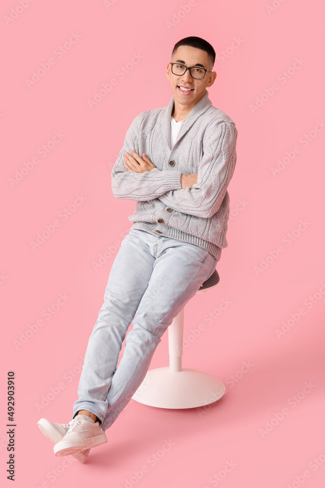 穿着针织毛衣的英俊亚洲年轻男子坐在粉色背景的椅子上