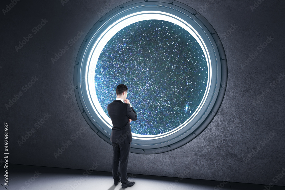 年轻商人从圆形照明器中向外看的背面视图，在conc中看到星空宇宙视图