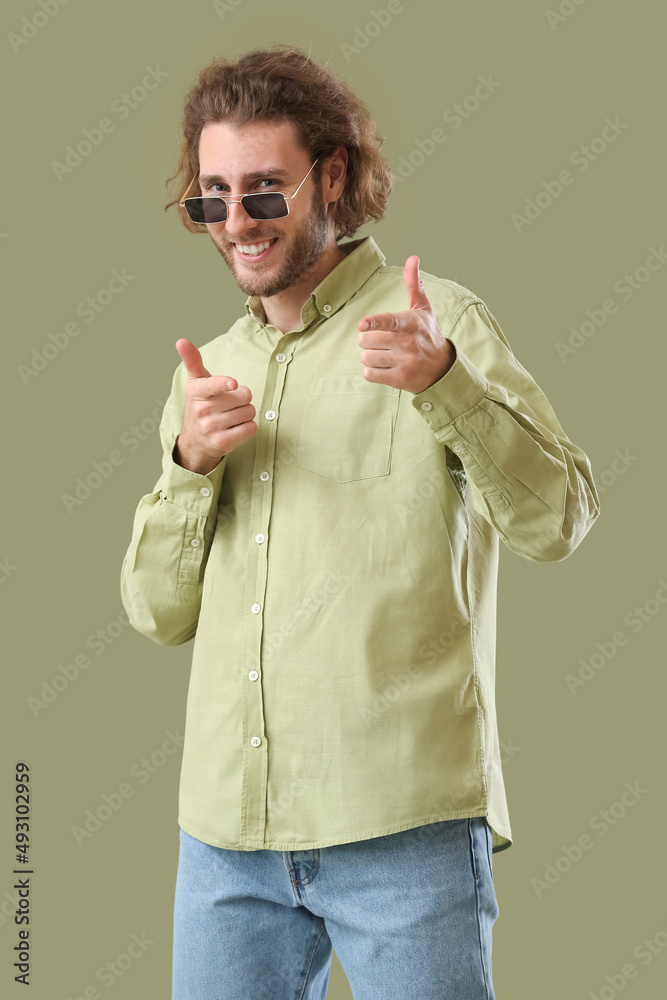 Handsome man in sunglasses pointing at viewer on green background