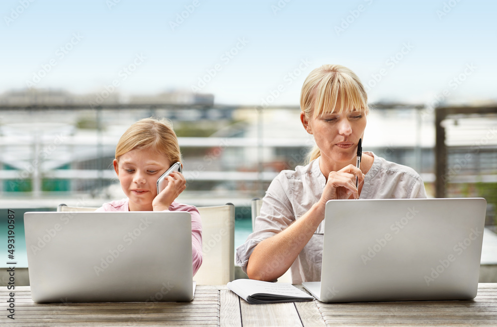 现在和未来的女商人。一个年轻女孩和她的母亲并排使用笔记本电脑的照片。