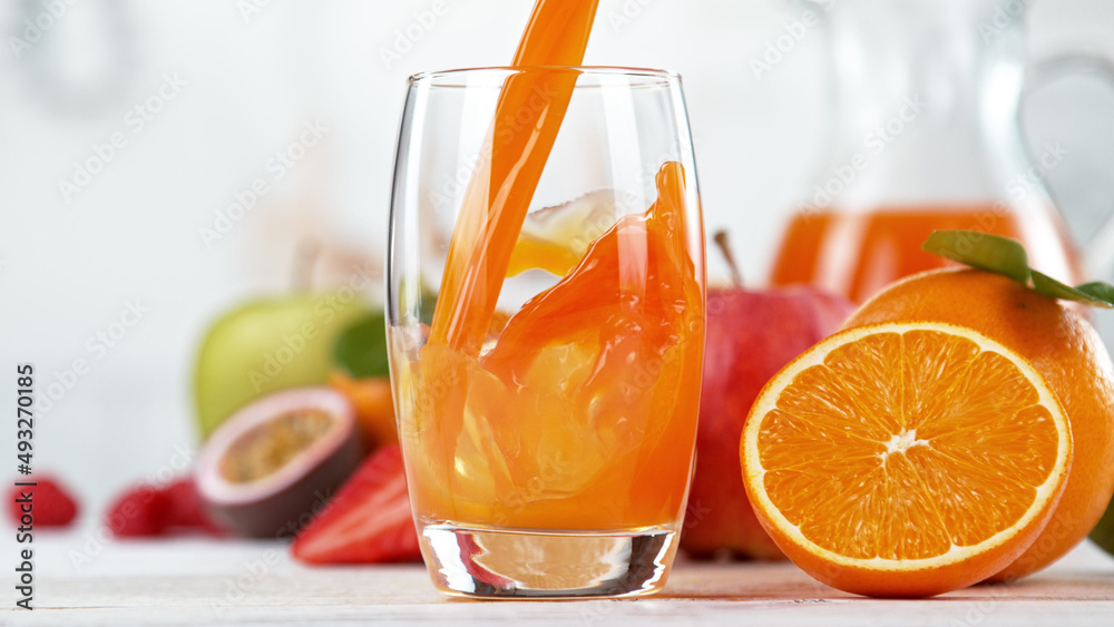 将多种维生素汁倒入玻璃杯。新鲜的橙汁和橙子水果放在厨房里。