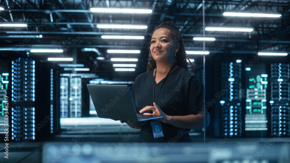 Portrait of Multiracial Mature Female IT Specialist Using Laptop, Standing in Data Center. Infrastru