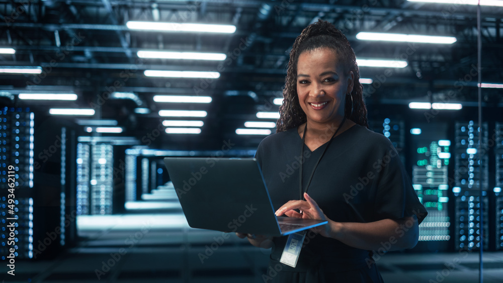 African American Female IT Specialist Using Laptop Computer, Standing in Big Warehouse Data Center. 